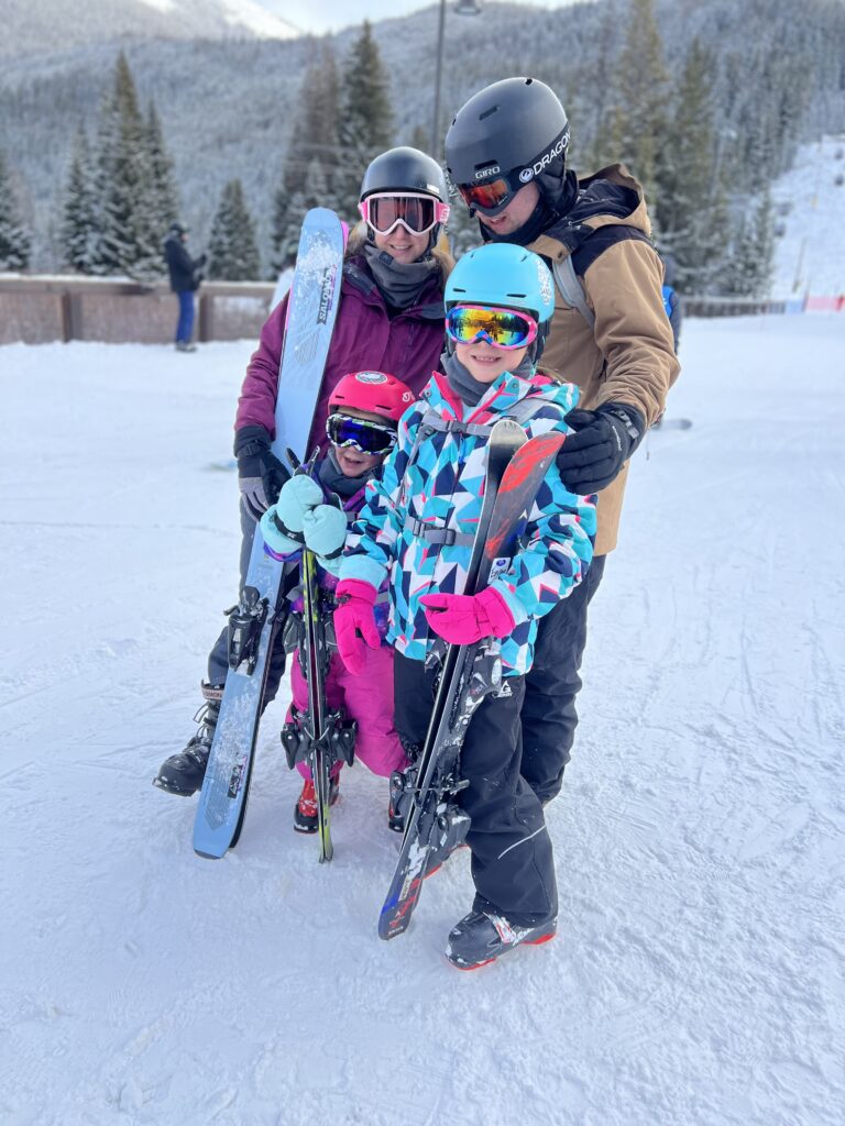 family photo at the bottom of a ski hill holding skis