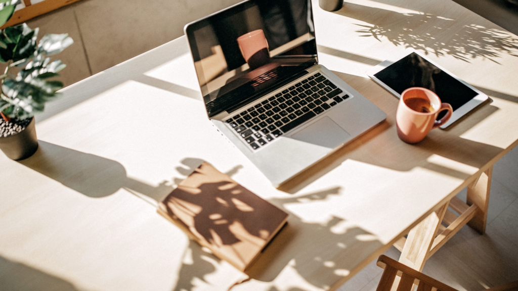 laptop and notebook on a desk with sun shining through a window.